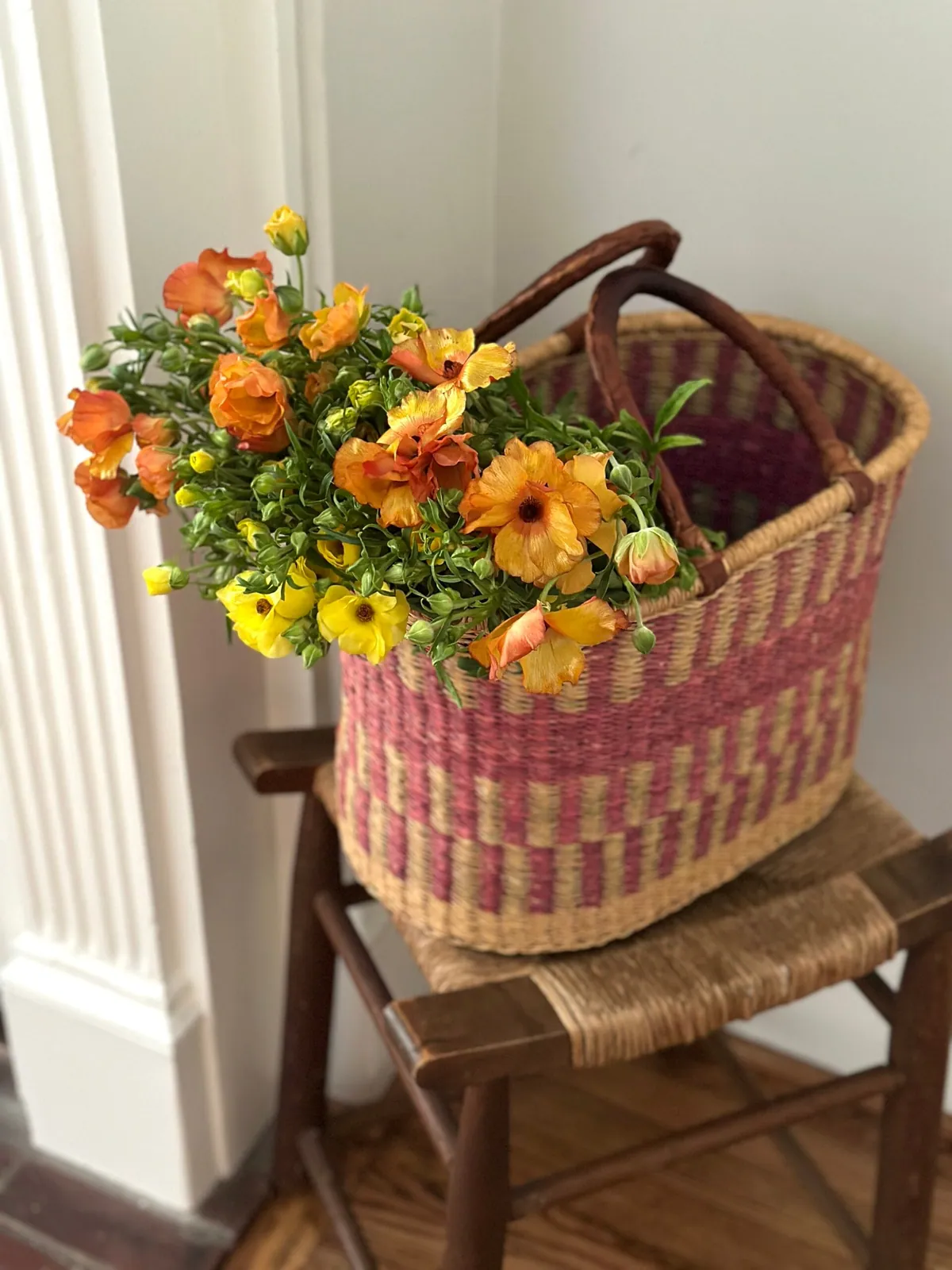 Woven basket of orange and yellow garden flowers on a rush-seat chair