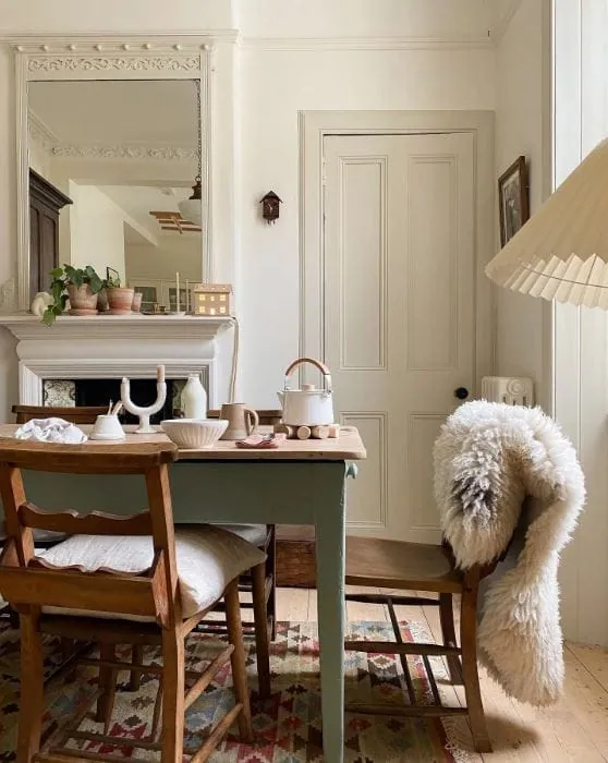 Dining room with a sage green painted table, mixed antique chairs and a layered rug