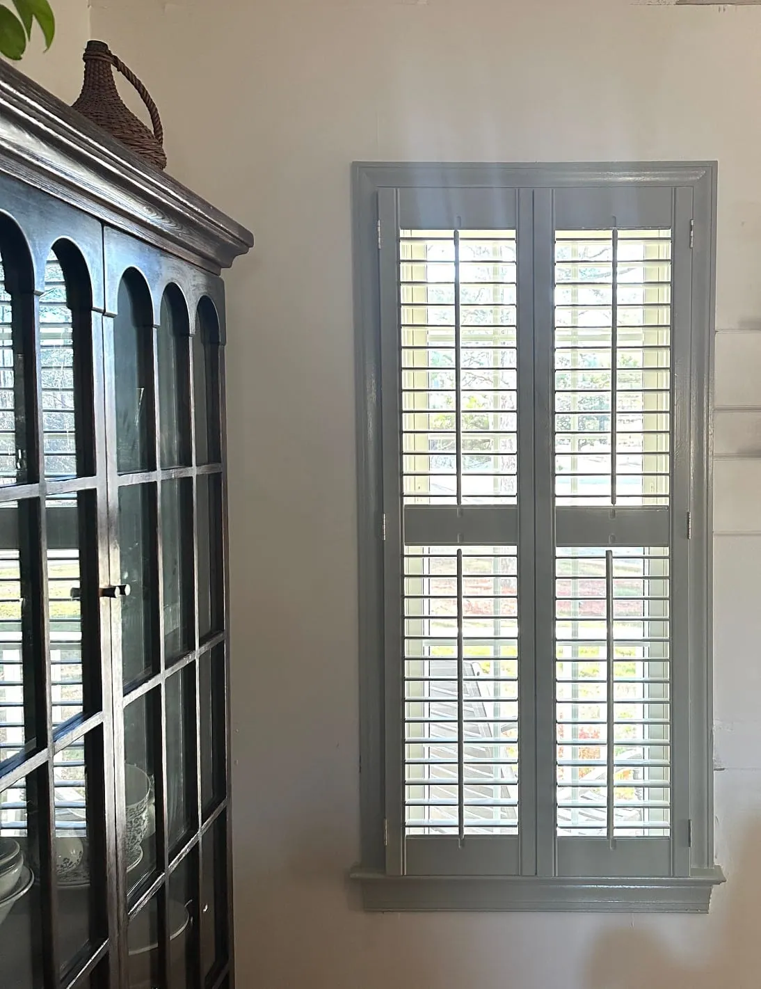 Plantation shutters painted soft green beside a dark glazed display cabinet