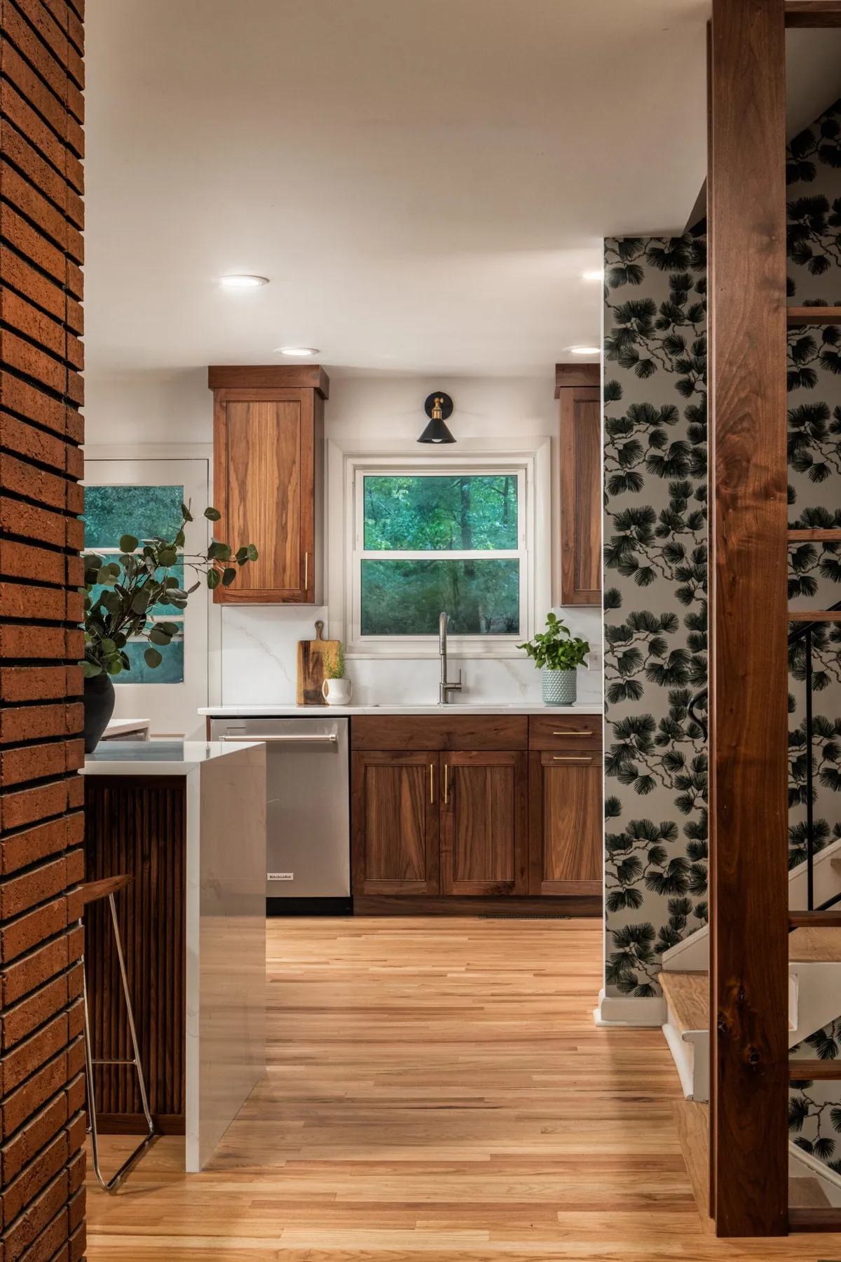 View through an exposed brick opening into a walnut and white kitchen