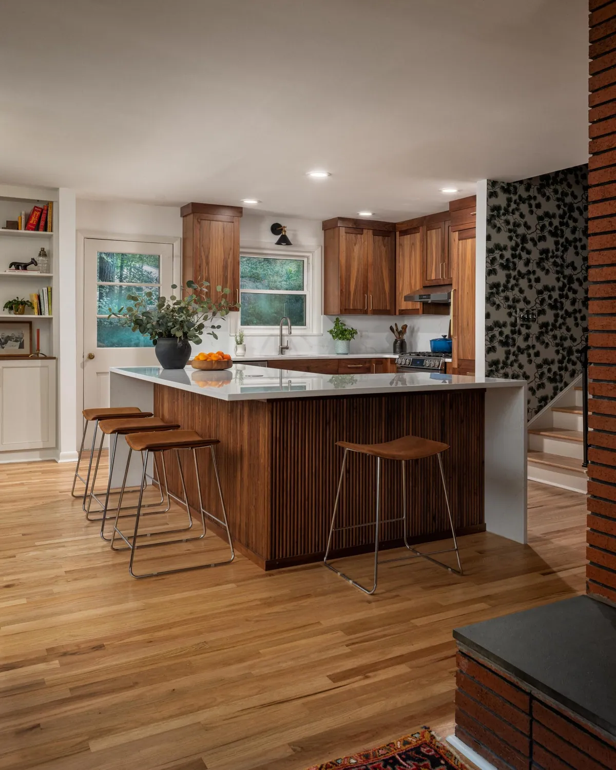 Walnut kitchen with a fluted island, counter stools and botanical wallpaper