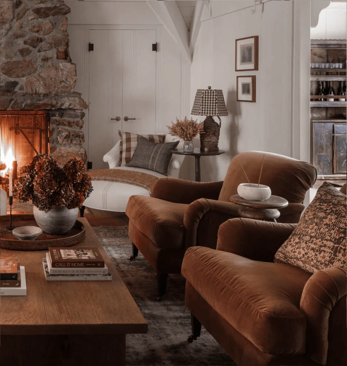 Autumn living room with rust velvet armchairs, dried hydrangeas and a lit stone fireplace