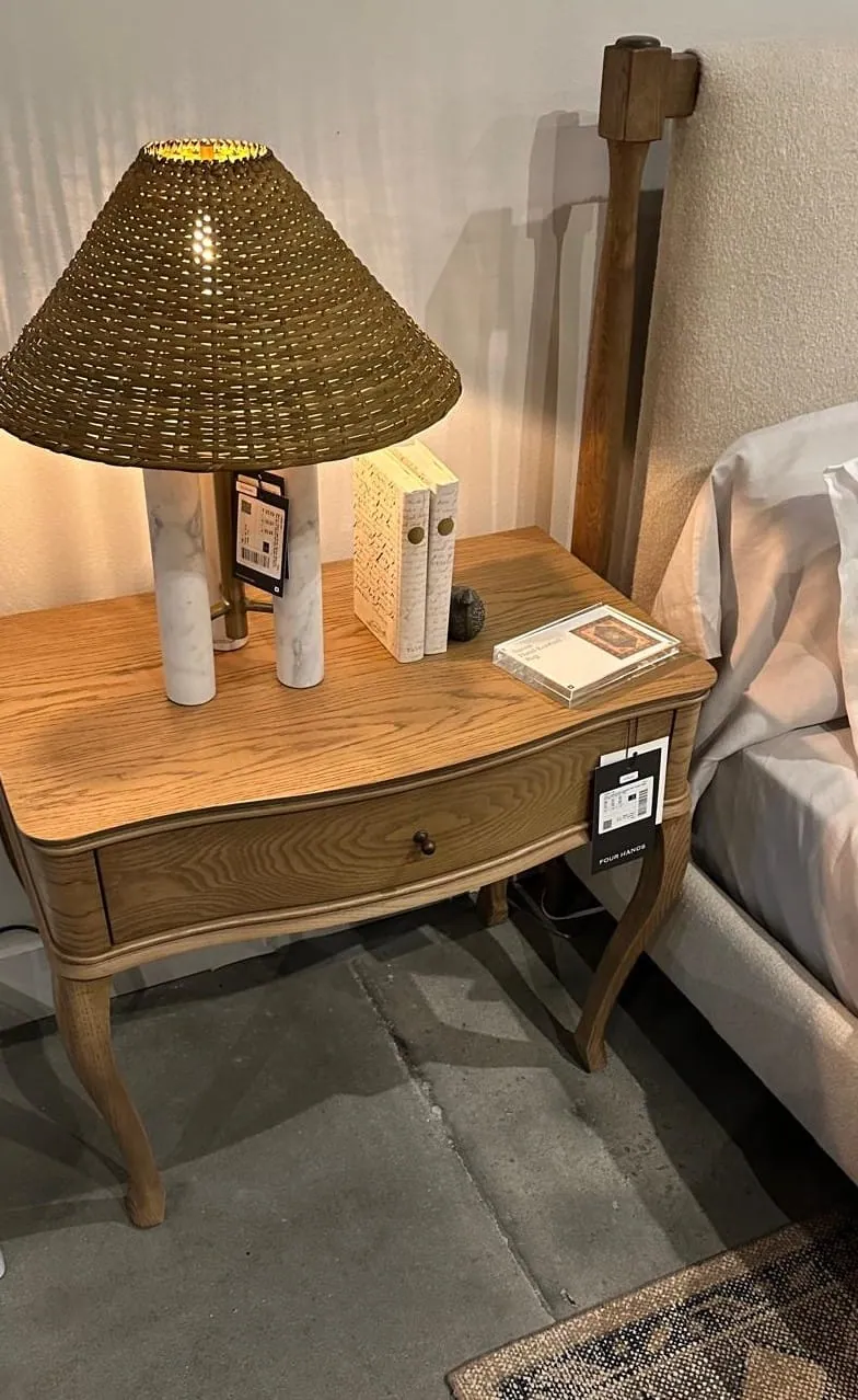 Woven shade lamp on a curved wood nightstand in a showroom bedroom