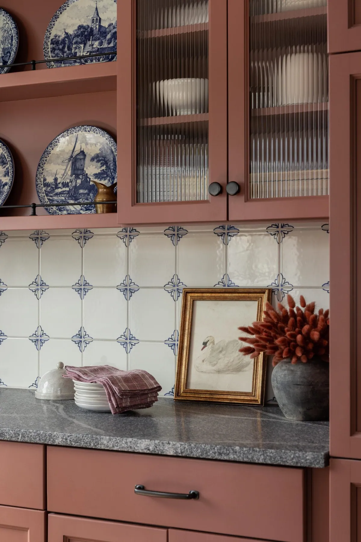 Blue and white transferware displayed in glass-front cabinets in a pink kitchen