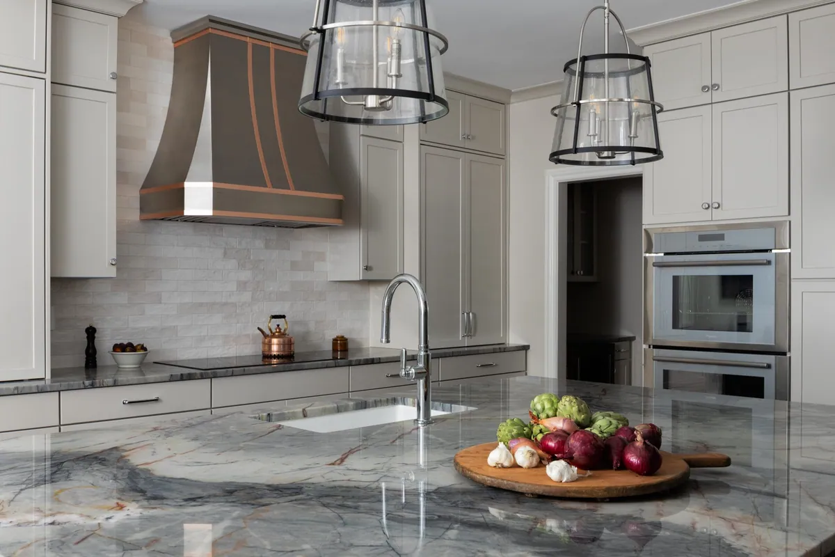 North Raleigh kitchen with a blue quartzite island, a custom metal range hood banded in copper, and glass lantern pendants