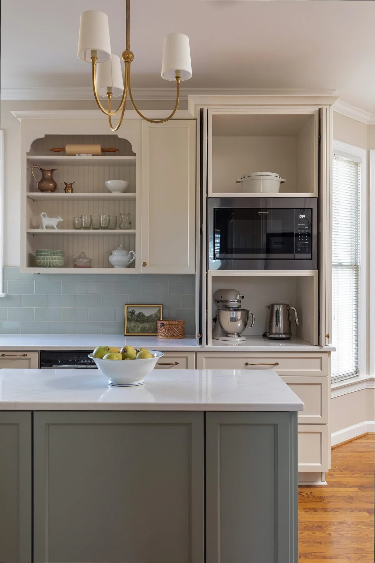Cream kitchen with a sage green island, glazed cabinetry and a pale blue tile backsplash