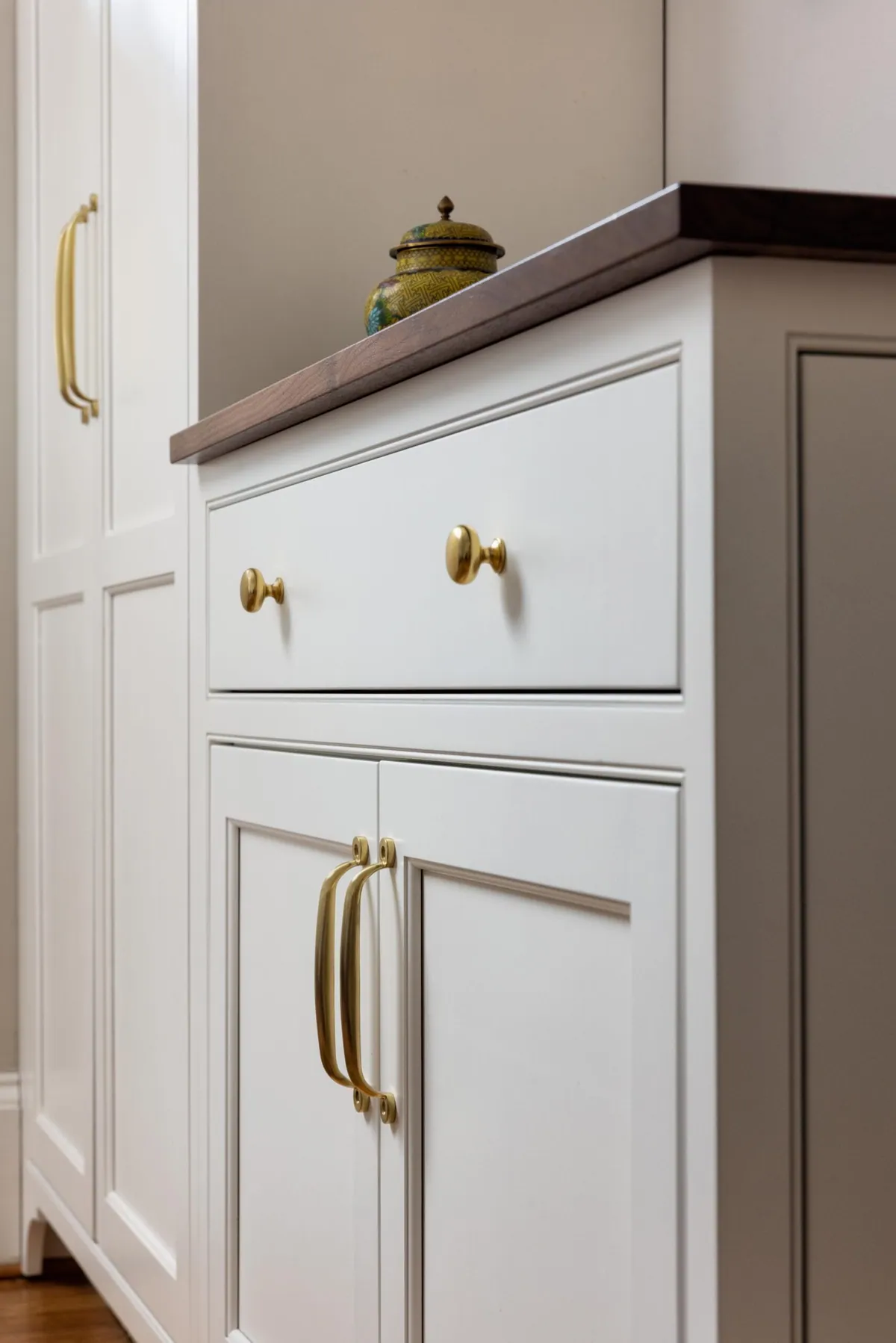 Pale green cabinetry with unlacquered brass pulls under a walnut counter