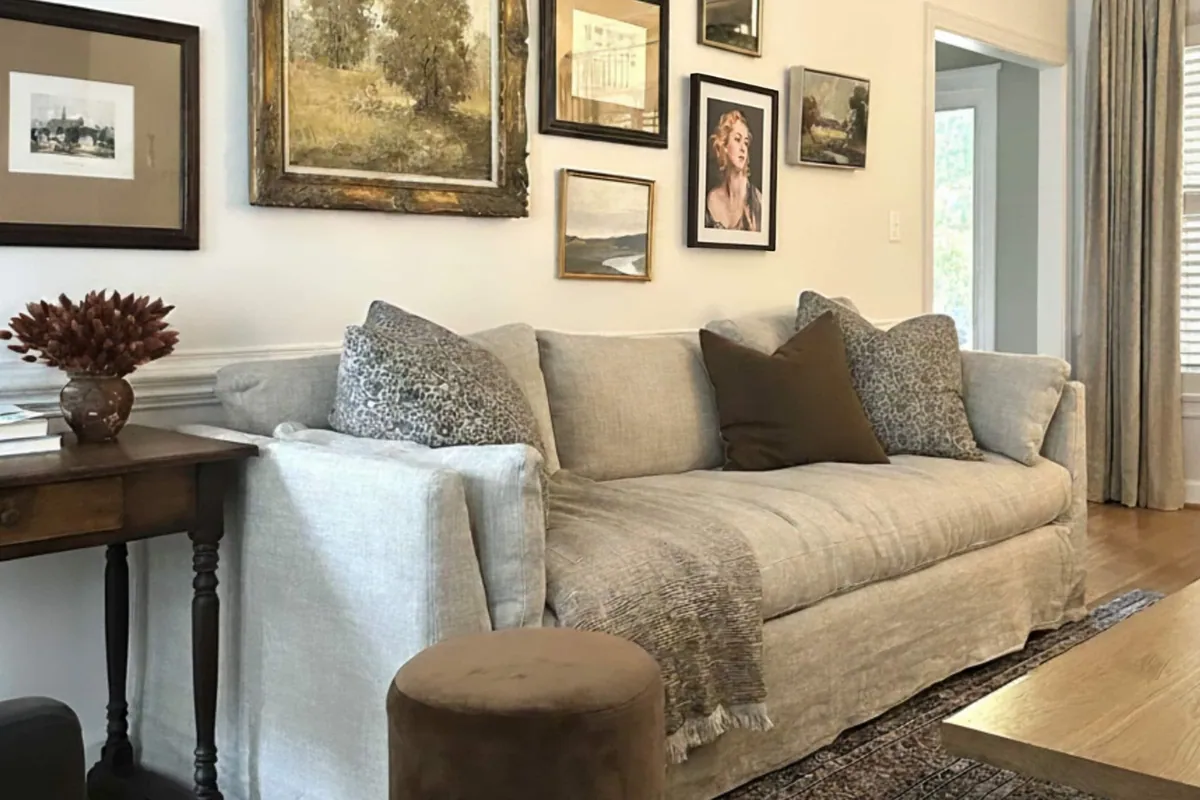 Living room with a linen slipcovered sofa and a gallery wall of framed landscapes