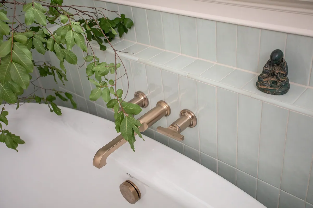 Aged brass tub filler against light green celadon tile