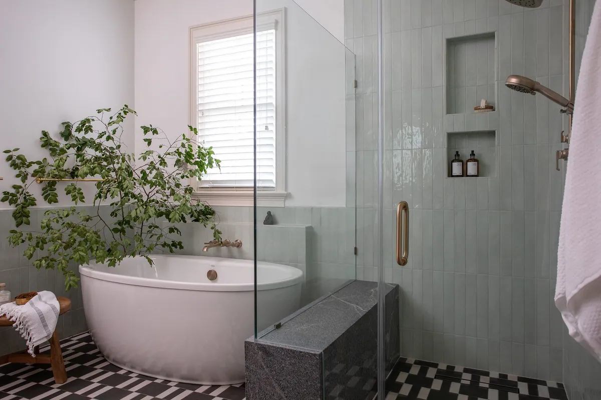 Bathroom with a freestanding oval tub, pale green vertical tile, a glass shower with a stone bench, brass fixtures and a black and white patterned floor