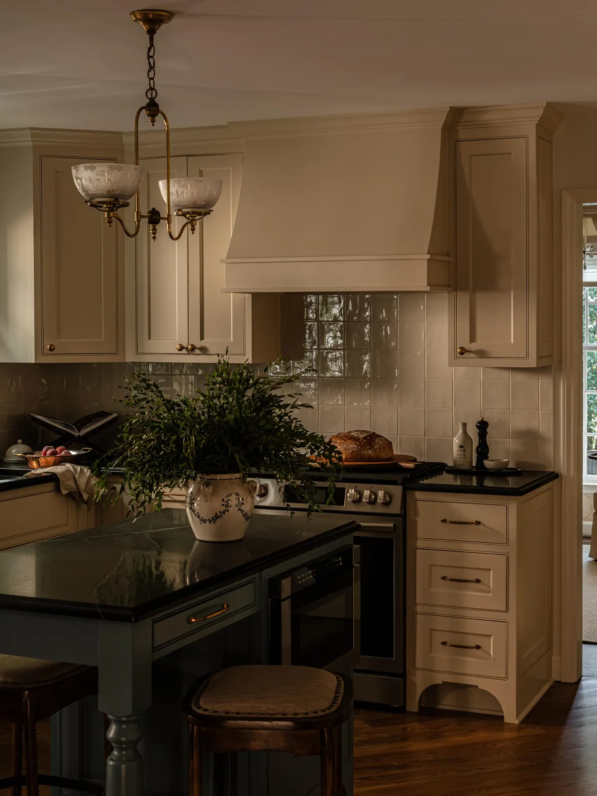 Custom hood and antique brass chandelier above a gray-blue kitchen island