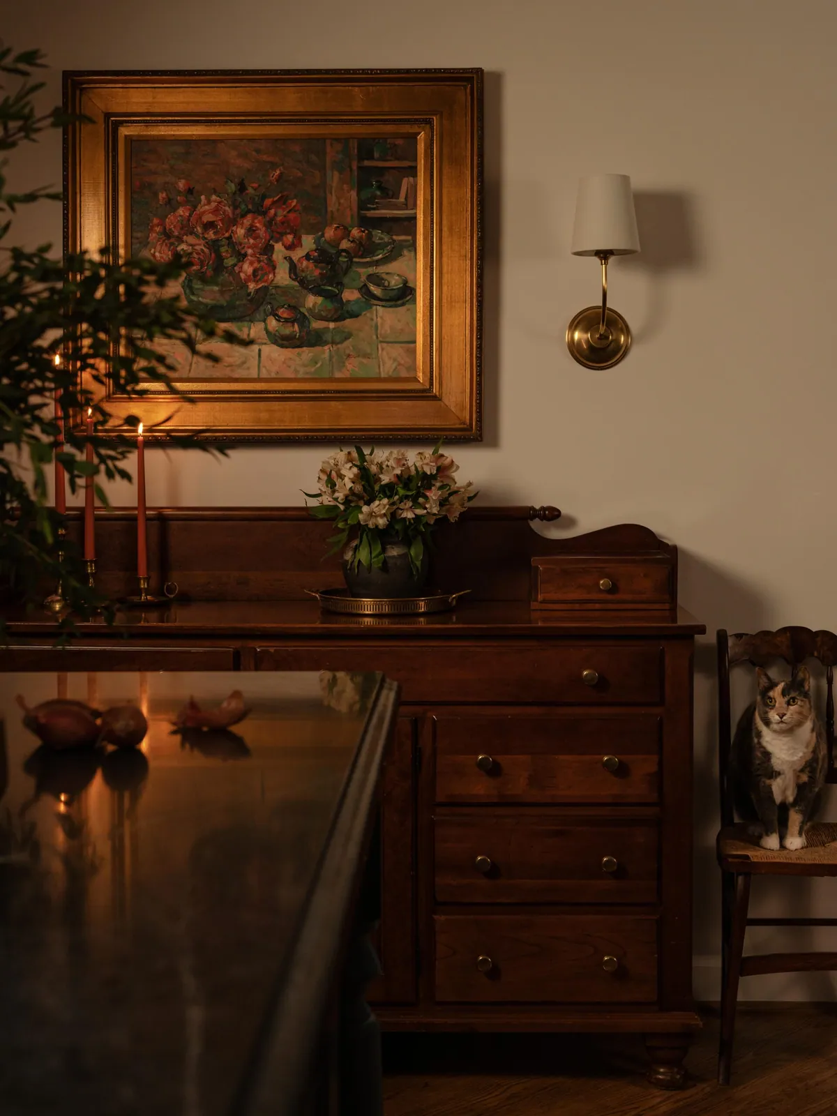 Antique wood chest with a gilt framed still life and brass sconce in the dining area