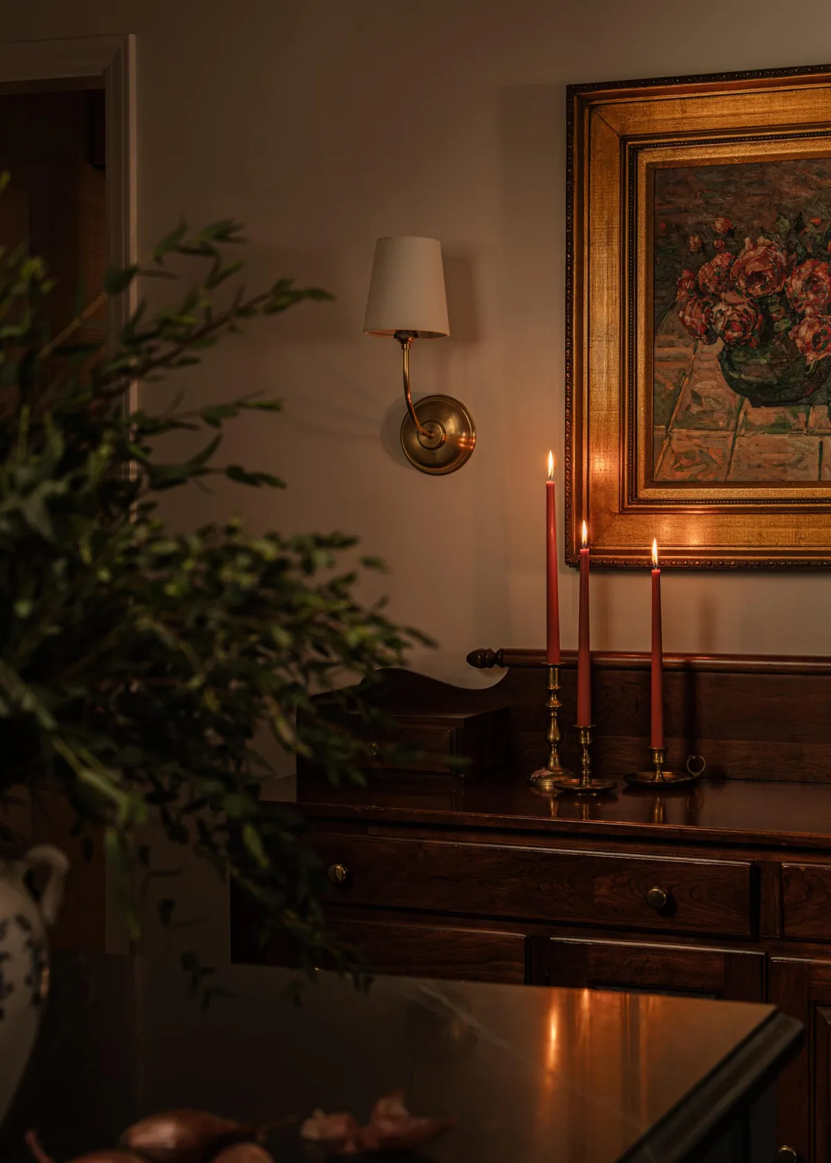 Brass sconce and taper candles beside a gilt framed painting