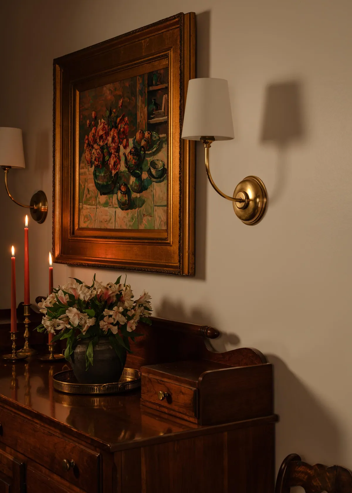 Pair of brass sconces flanking a gilt framed floral painting above an antique chest
