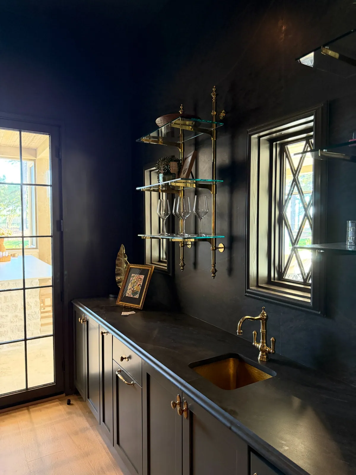 Brass and glass shelves across a dark bar wall above a black countertop