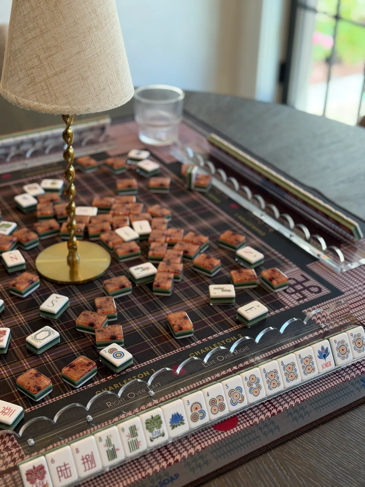 Mahjong tiles laid out on a game table beside a brass lamp