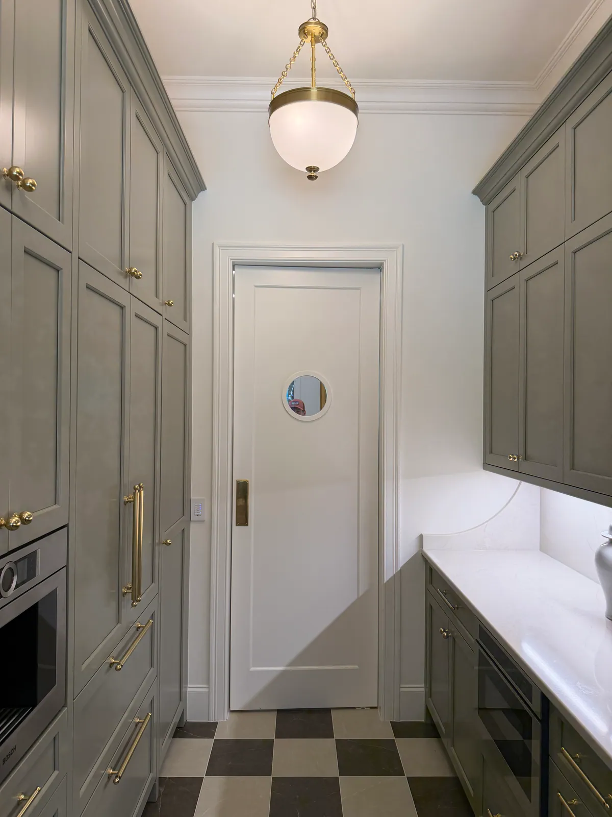 Scullery with gray green cabinets, a checkered floor and a porthole window in the door