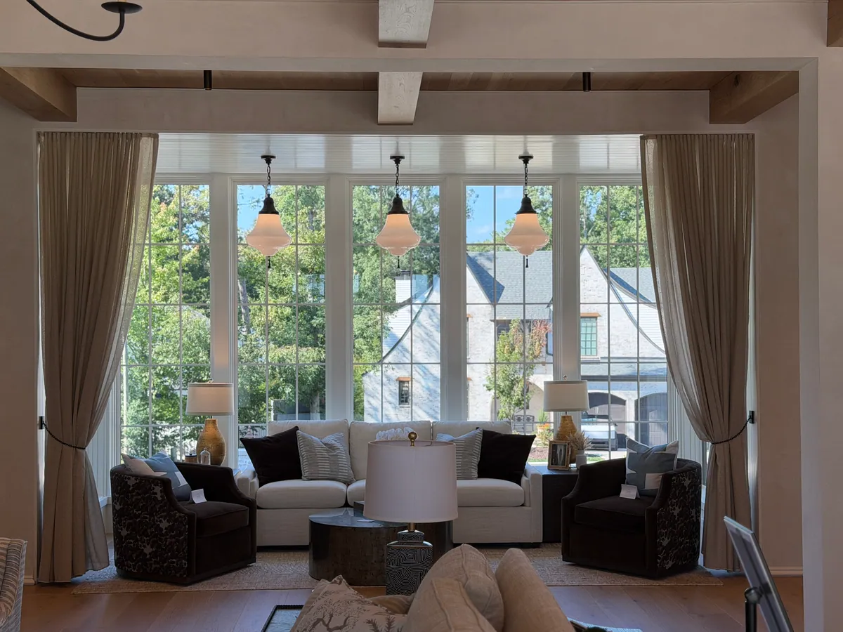 Living room with linen drapery tied back on either side of a wall of windows, under three glass pendants