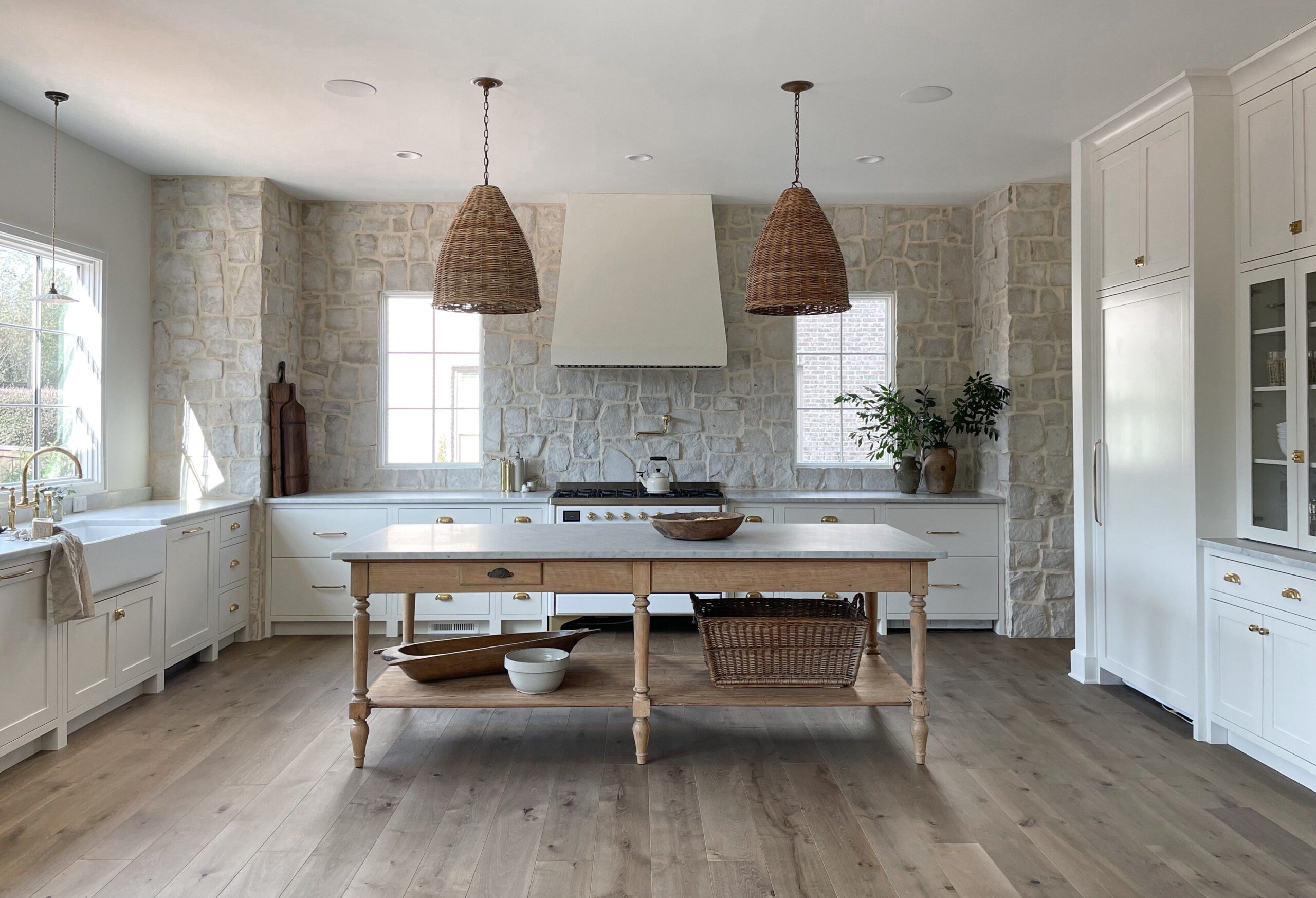 rustic charming cottage kitchen, stone accent wall, woven rattan island pendants, white kitchen cabinetry, vintage island table