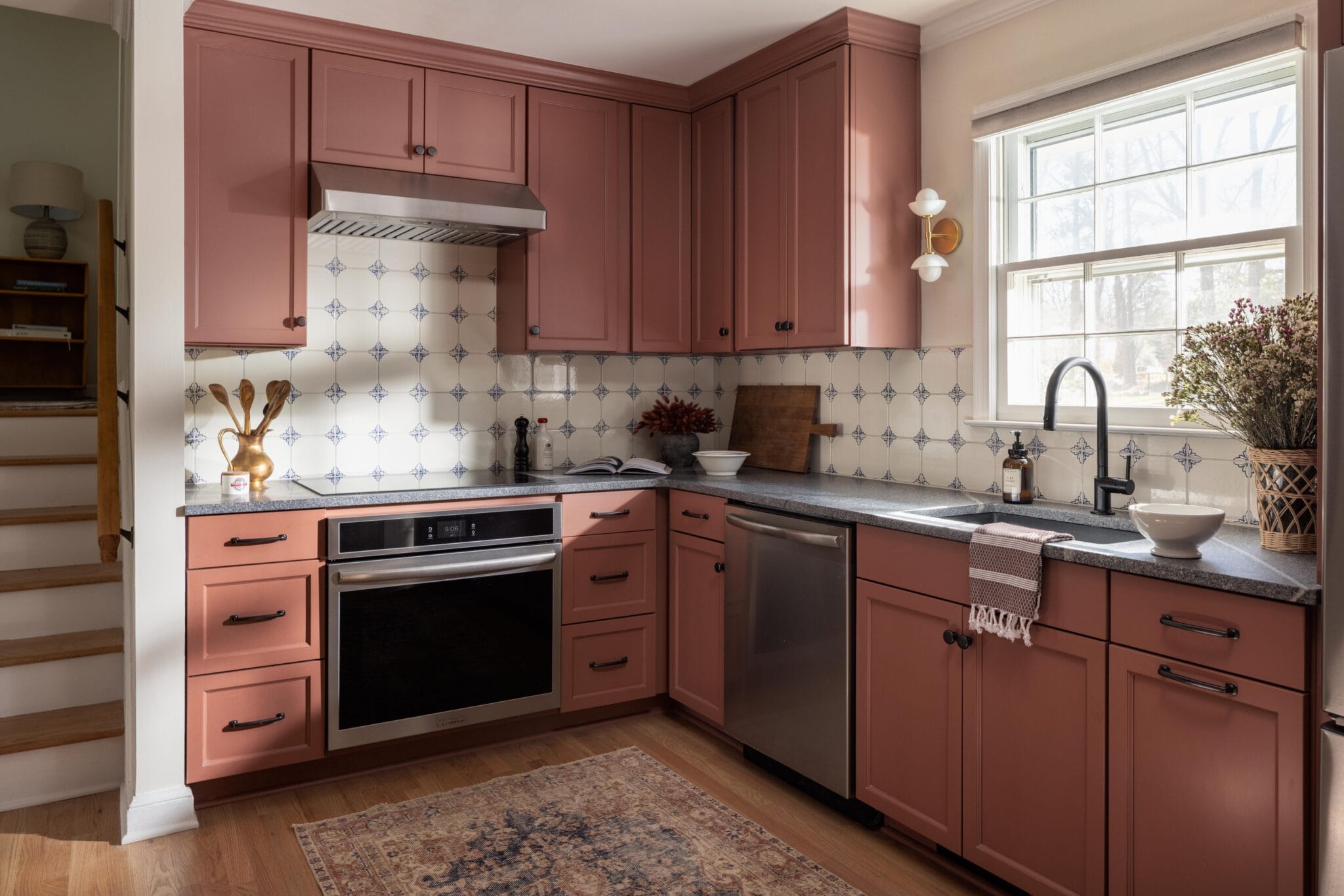 Kitchen with terracotta cabinets, patterned blue and cream tile backsplash and black hardware