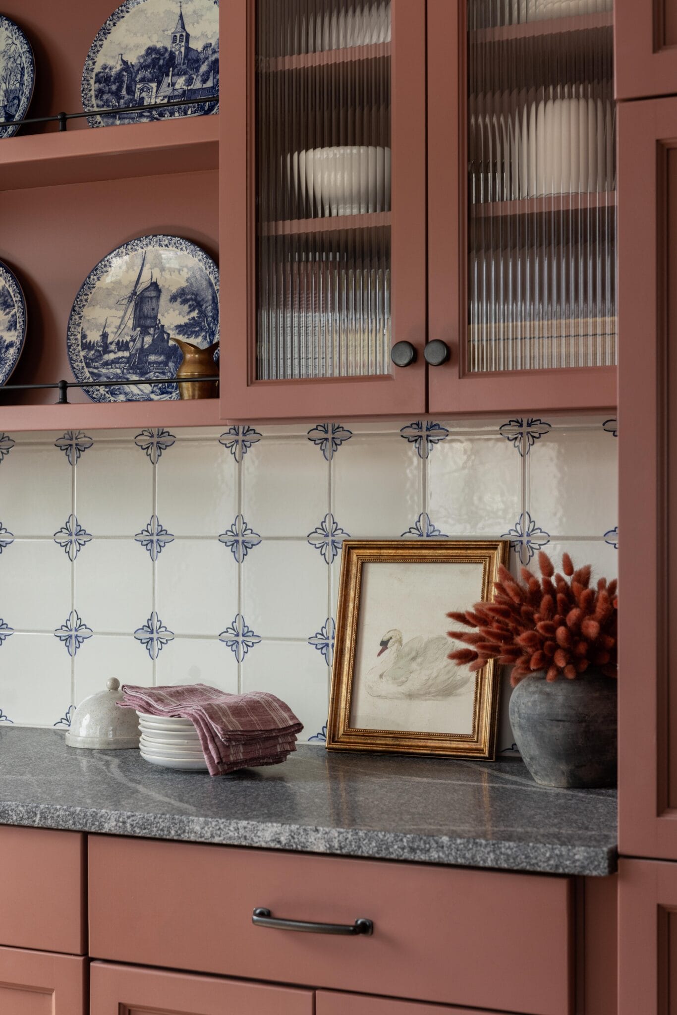 Blue and white transferware displayed in glass-front cabinets in a pink kitchen