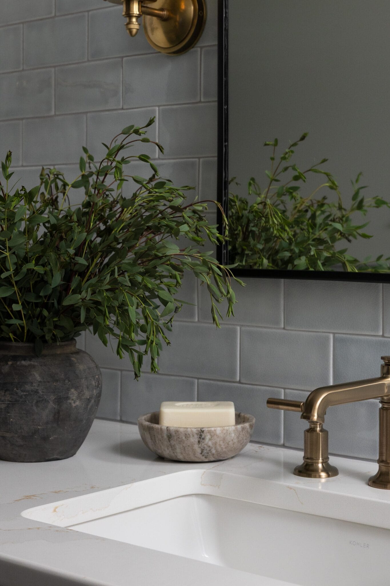 Bathroom vanity with gray subway tile, an unlacquered brass faucet and a stone soap dish