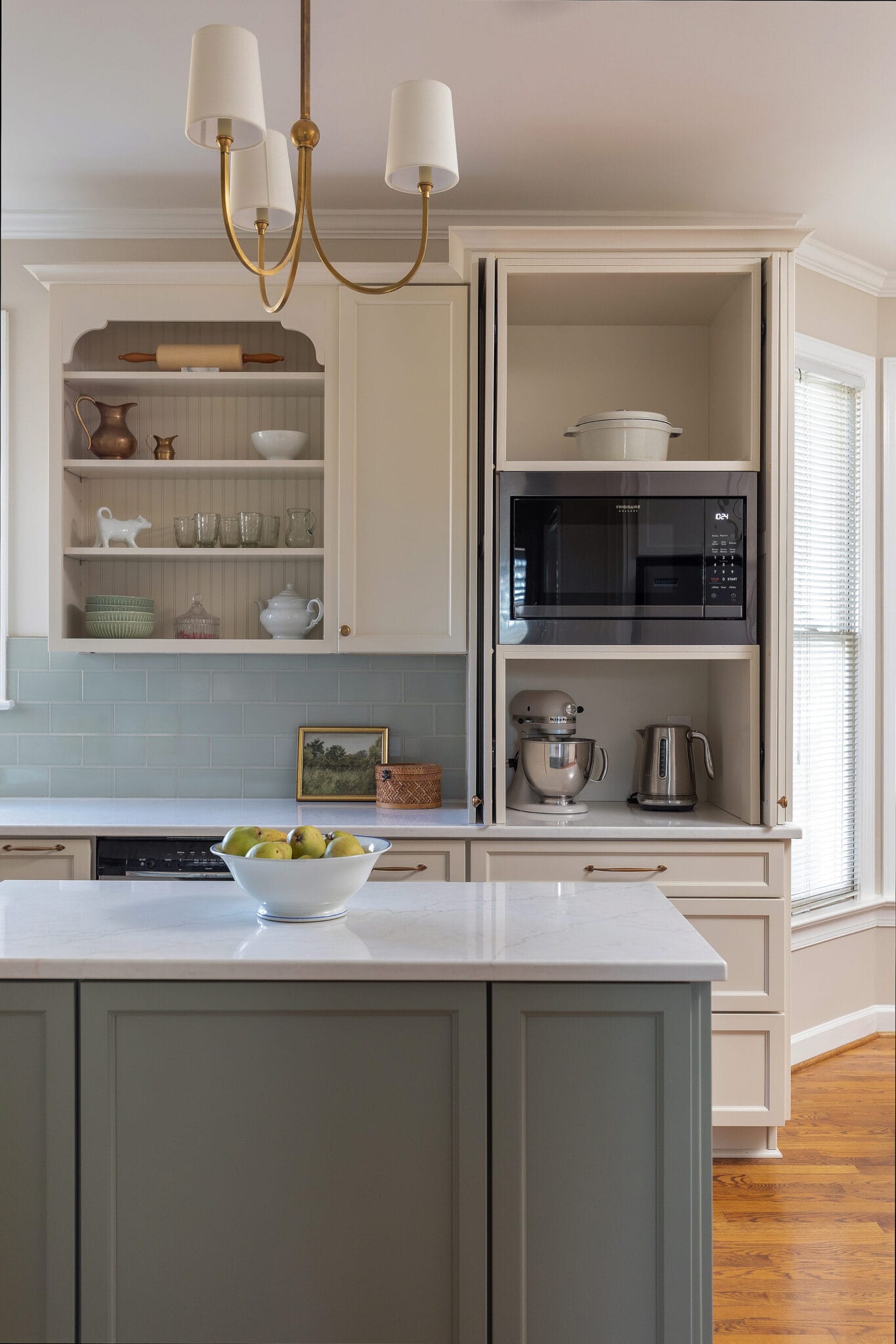 Cream kitchen with a sage green island, glazed cabinetry and a pale blue tile backsplash