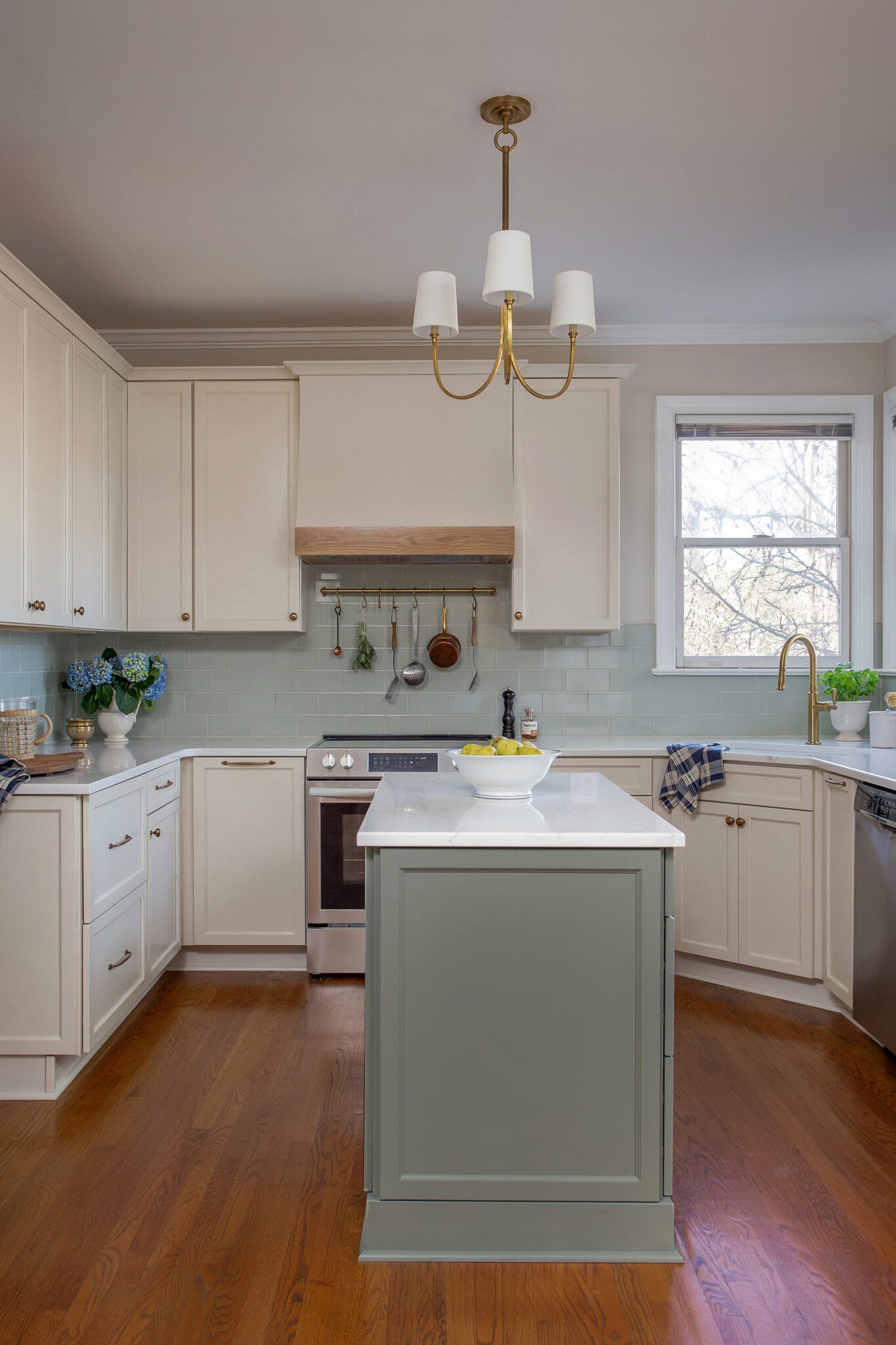 Cream kitchen with a sage green island, brass chandelier and quartz counters