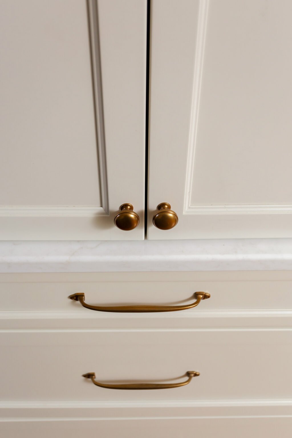 close up of aged brass cabinet hardware with creamy kitchen cabinets