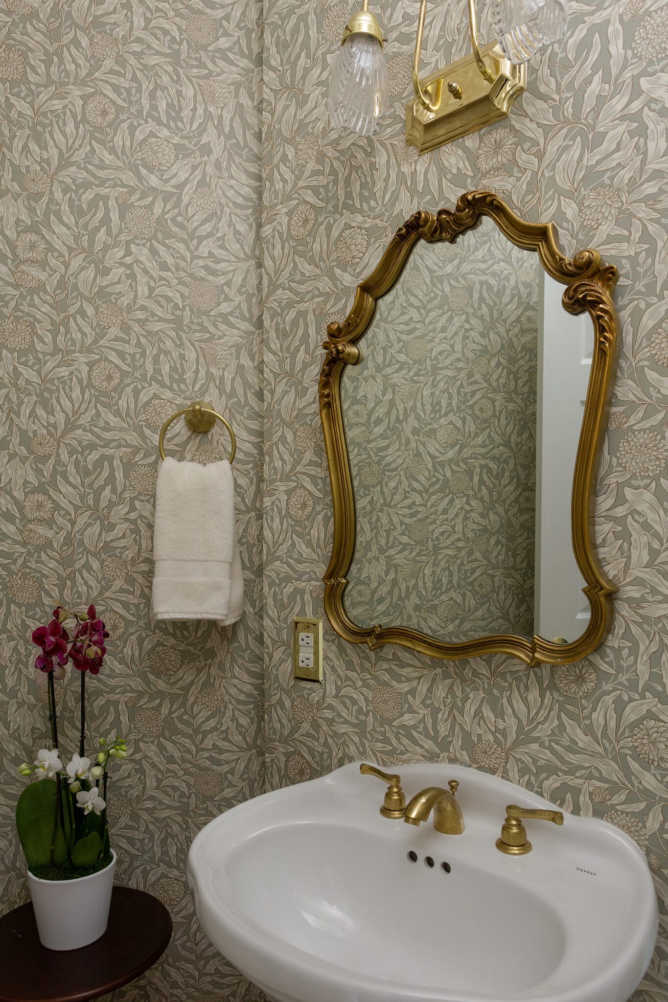 Powder room with botanical wallpaper, a gilt mirror and a brass widespread faucet